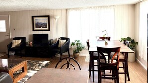 A living room with a sofa, a coffee table, a TV, and a dining area with chairs and a table. - Charming Apartment in Downtown Lyons! 3bed/2bath (Lyons)