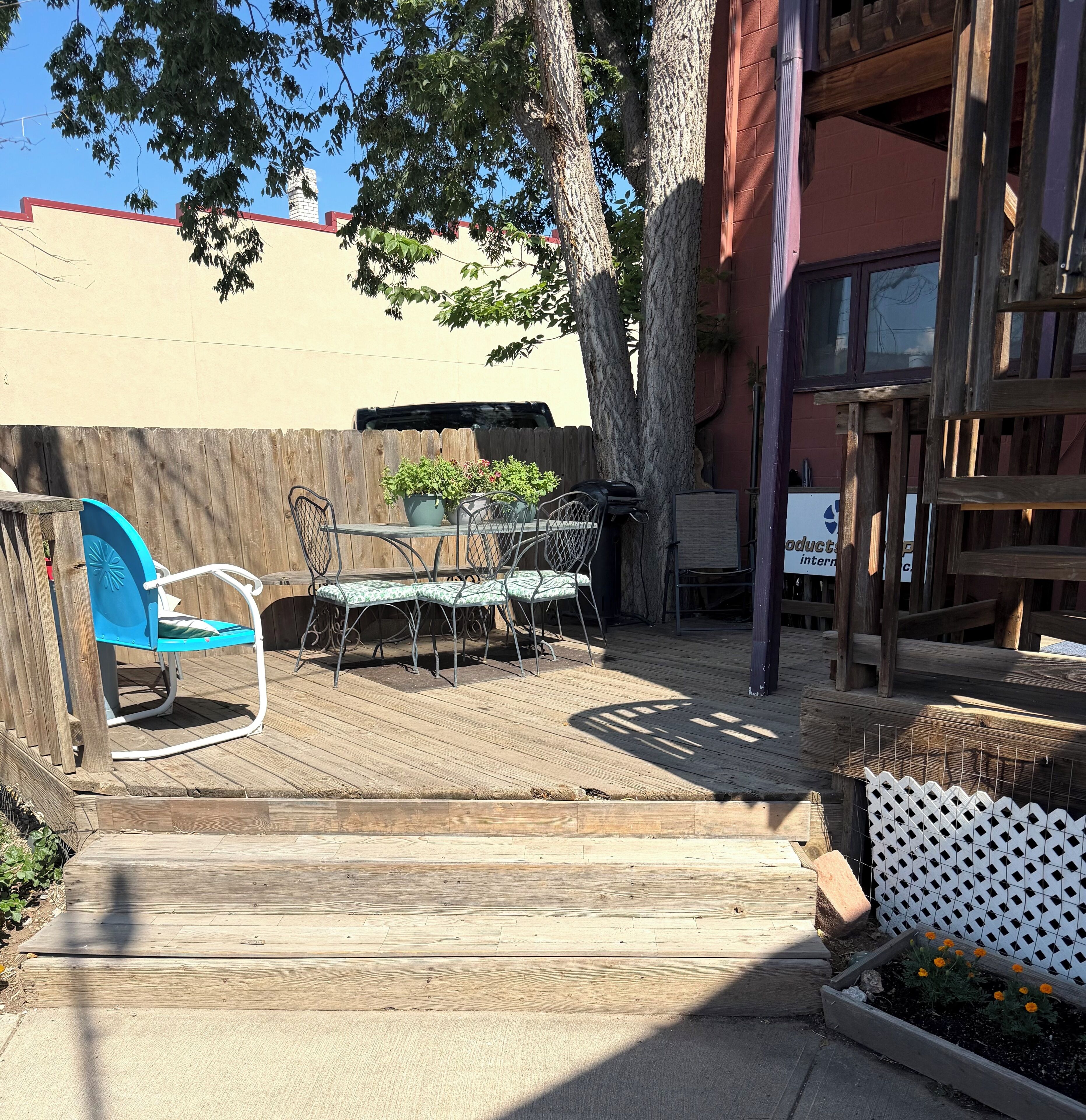 A wooden deck with outdoor furniture, a white picket fence, and a garden bed with flowers.