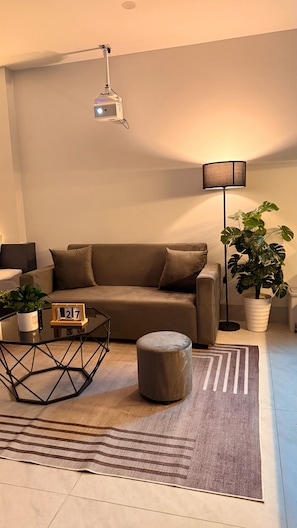 Una sala de estar con sofá, mesa de centro, lámpara, planta en maceta y alfombra.