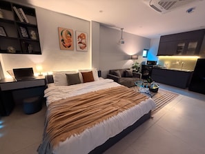 A modern bedroom with a large bed, a desk with a laptop, a sofa, and a kitchenette area. -  Modern Balcony Studio 5 mins to Hanoi Station (Hà Nội)