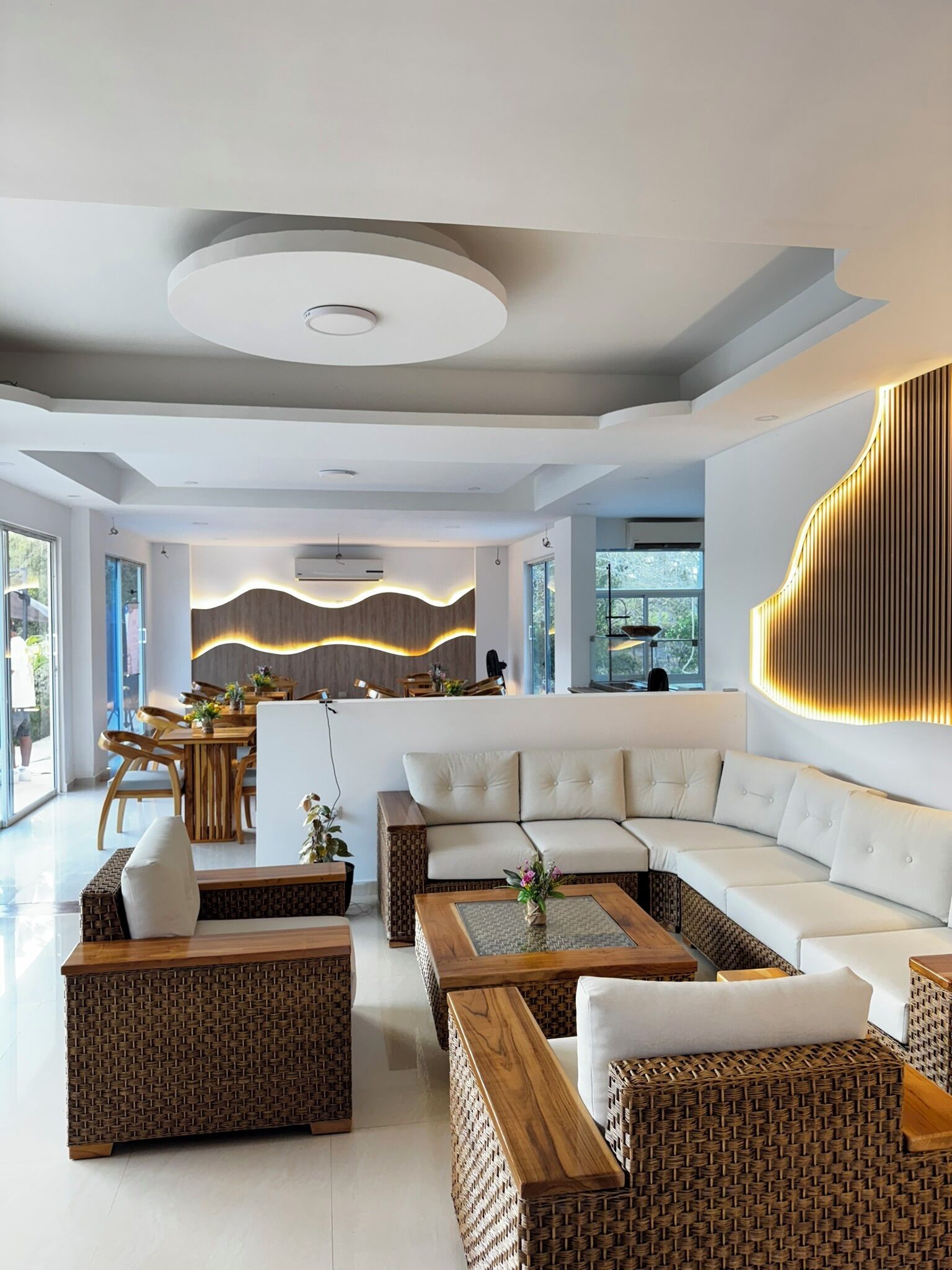 A modern living room with a sectional sofa, wicker furniture, and a kitchen area in the background.