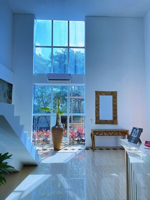 A spacious room with a large window, a potted plant, a wooden bench, and a decorative mirror.