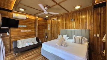 A hotel room with a wooden interior, a bed with white bedding, a grey headboard, and a ceiling fan.