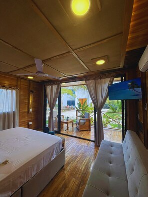 A room with a bed, a sofa, a ceiling fan, and a television.