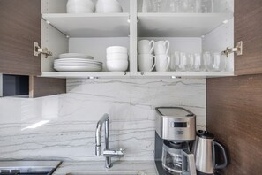 A kitchen with a marble countertop, a coffee maker, and a cabinet with dishes and glasses. - Blueground | Lenox Hill, view, nr Central Park (New York)