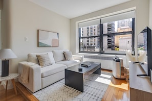 A modern living room with a sofa, coffee table, and a large window with a view of buildings. - Blueground | Lenox Hill, view, nr Central Park (New York)