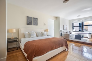 A modern bedroom with a large bed, bedside tables, a sofa, and a view of the city through large windows. - Blueground | Lenox Hill, view, nr Central Park (New York)