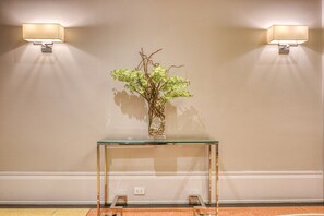 A glass console table with a vase of green foliage against a wall with two wall-mounted lights. - Blueground | Lenox Hill, view, nr Central Park (New York)