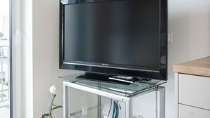 Ein Flachbildfernseher auf einem Glasständer mit Fernbedienung, platziert in der Nähe eines Fensters.