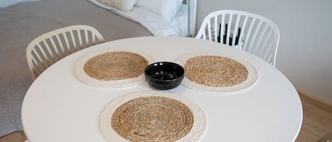 A round table with a white surface and four woven placemats. A black bowl is placed in the center.