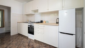 Een keuken met witte kastjes, een fornuis, oven en een koelkast.