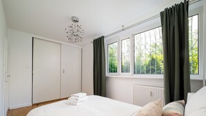 Een slaapkamer met een bed, een radiator, een raam met gordijnen en een deur.