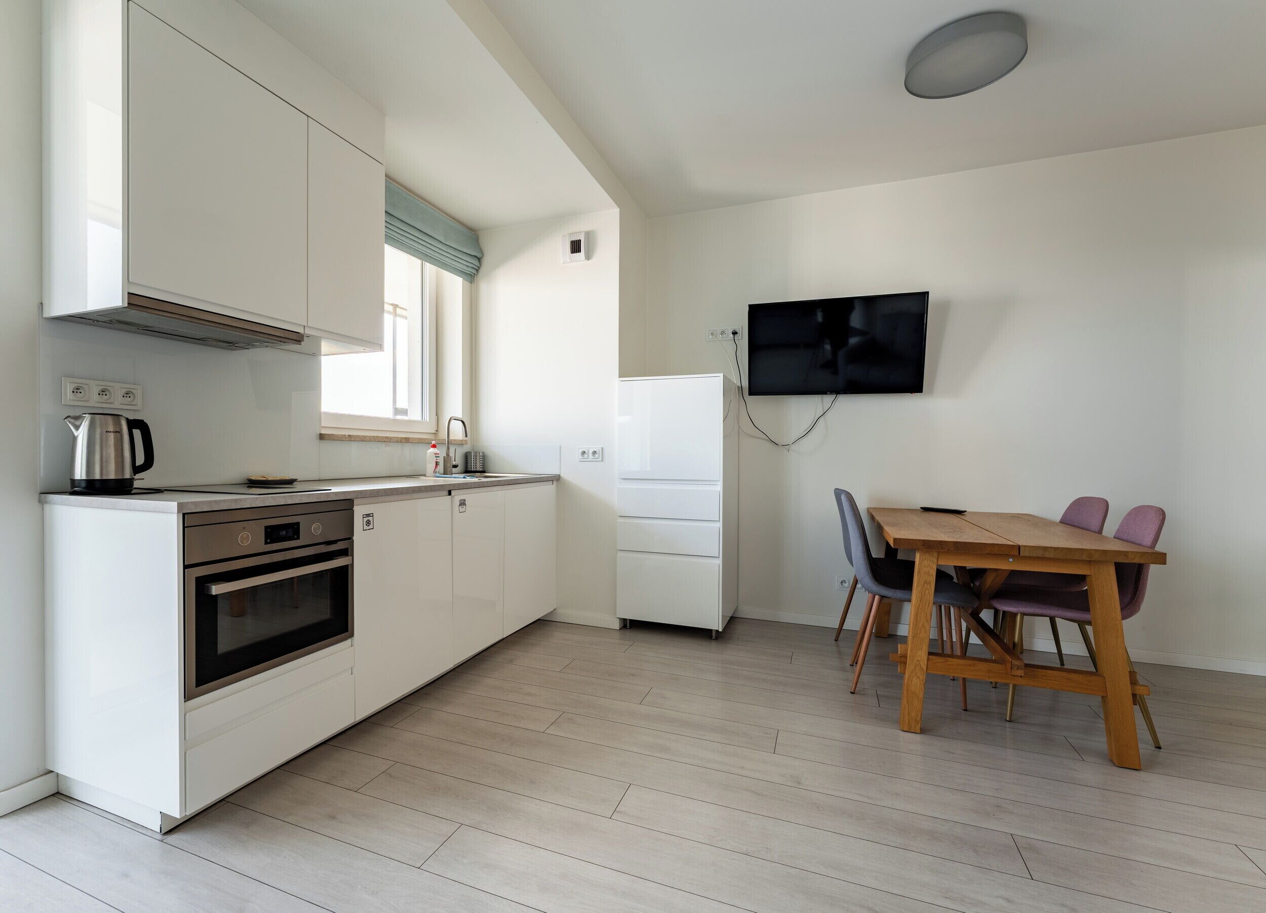 Una cocina compacta con horno integrado, cafetera y comedor con mesa y sillas de madera.