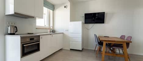 A compact kitchen with a built-in oven, a coffee maker, and a dining area with a wooden table and chairs.