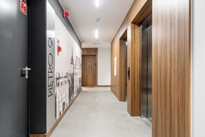 A modern hotel corridor with wooden paneling, a tiled floor, and a wall-mounted fire alarm. - Bastion Wałowa Skyline Apartment #1 (Gdańsk)