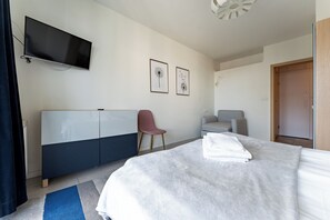 Ein modernes Hotelzimmer mit Bett, Schreibtisch, Stuhl, Fernseher und zwei gerahmten Bildern an der Wand.
