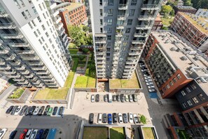 En høj boligbygning med flere balkoner, en tagterrasse og en parkeringsplads med biler.