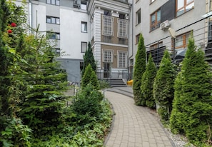 Ein Weg führt zu einem Gebäude mit einer Treppe, umgeben von Grünflächen und Blumentöpfen.