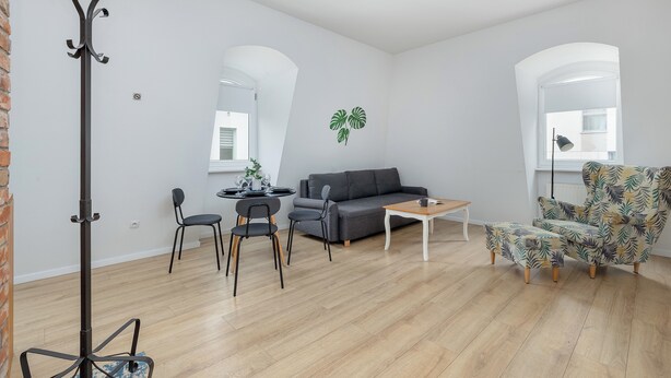 A modern living room with a grey sofa, a patterned armchair, a dining table with chairs, and a tall floor lamp. - Targ Rybny Riverside Apartment (Szczecin)