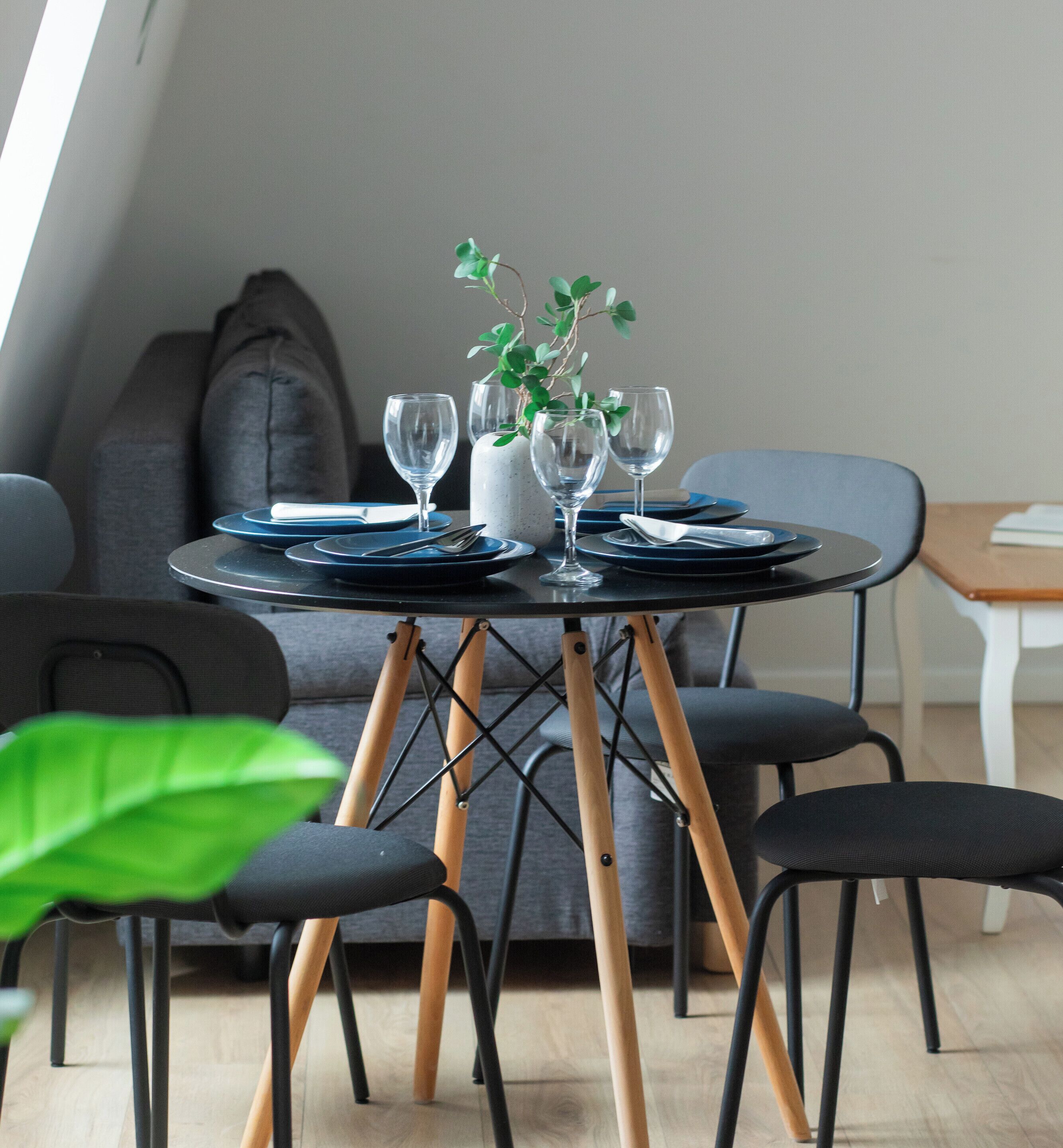 Ein Esstisch mit Tellern, Besteck und Gläsern, in einem Raum mit grauem Sofa und Sesseln.