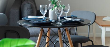 A dining table with plates, cutlery, and glasses, set in a room with a grey sofa and chairs.