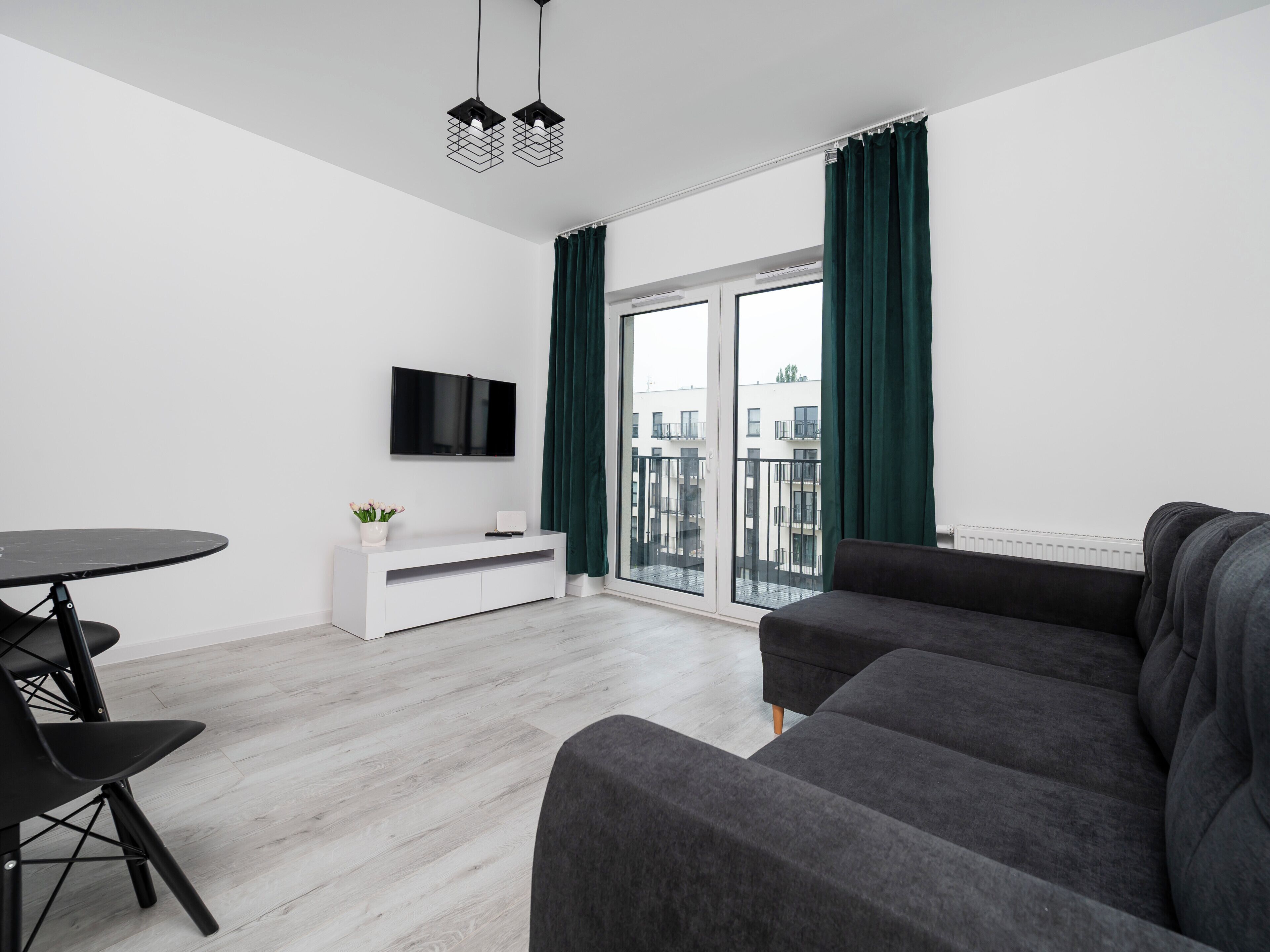 Una sala de estar moderna con un sofá gris, un mueble blanco para televisión y una mesa de comedor con sillas.