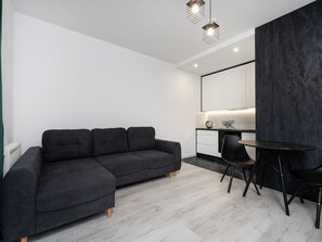 A modern living space with a sectional sofa, a dining table with chairs, a kitchen area, and a large mirror. - 1 Maja Prestige Studio (Łódź)