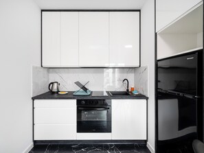 A compact kitchen with white cabinets, a black countertop, a built-in oven, and a microwave. - 1 Maja Prestige Studio (Łódź)