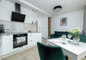A modern kitchen with white cabinetry, a built-in oven, and a black range hood. - Szczecin Bronowicka Malachite Studio (Szczecin)
