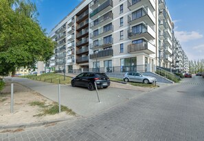 Ein mehrstöckiges Wohngebäude mit Balkonen, einem gepflasterten Fußgängerbereich und parkenden Autos.