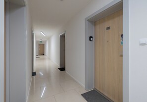 Ein Hotelgang mit einer Holztür mit der Beschriftung '117', einem Lichtschalter und einem kleinen Schild an der Wand.