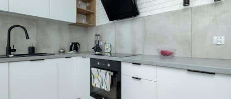 A modern kitchen with white cabinets, a black range hood, and a built-in oven.