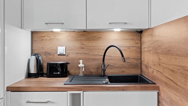 A modern kitchen with a wooden backsplash, a black sink, and stainless steel appliances. - Pagi City Comfort Apartment with Garden (Lublin)