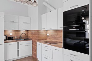 A modern kitchen with white cabinetry, a wooden backsplash, and a black Bosch oven. - Pagi City Comfort Apartment with Garden (Lublin)