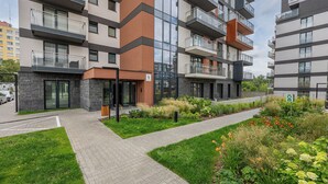 A multi-story residential building with balconies, a paved entrance, and a landscaped garden area. - Pagi City Comfort Apartment with Garden (Lublin)