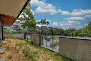 Blick auf ein modernes Gebäude mit Betonfassade, eine umzäunte Grünfläche und einen klaren Himmel.