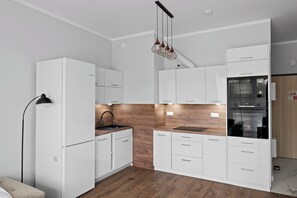 Eine moderne Küche mit weißen Schränken, einer Holz-Spritzschutzwand und einer schwarzen Pendelleuchte.