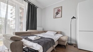 A modern bedroom with a sofa bed, a bedside table, a floor lamp, and a window with curtains. - Pagi City Comfort Apartment with Garden (Lublin)