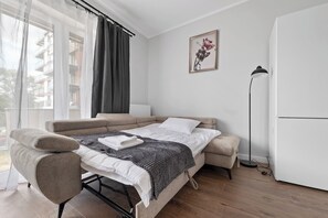 Ein modernes Schlafzimmer mit Schlafsofa, Nachttisch, Stehlampe und einem Fenster mit Vorhängen.
