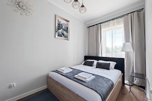 A modern bedroom with a bed, a bedside table, a lamp, and a window with curtains.