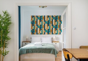 A hotel room with a bed, two bedside tables, a lamp, a chair, and a large abstract painting on the wall. - Nowy Świat Central Apartment (Warszawa)