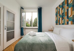Un dormitorio con cama, ventana con cortinas, radiador y pared con diseño geométrico.