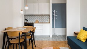 A modern kitchen with white cabinets, a wooden dining table, and a coffee maker. - Nowy Świat Central Apartment (Warszawa)