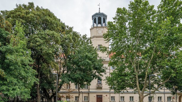 A building with a clock tower, surrounded by trees and a paved walkway with benches. - Nowy Świat Central Apartment (Warszawa)