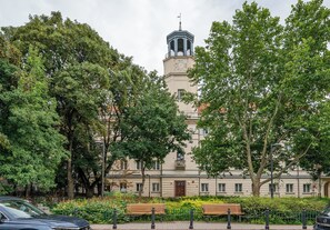 Un bâtiment doté d’une tour horloge, entouré d’arbres et bordé d’une promenade pavée avec des bancs.