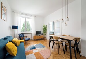 A modern living room with a sofa, a dining table, and a TV. - Nowy Świat Central Apartment (Warszawa)