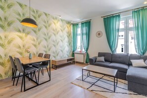 A living room with a sofa, coffee table, dining table with chairs, and a radiator. - Mikołowska Silesian Charm Apartment (Katowice)