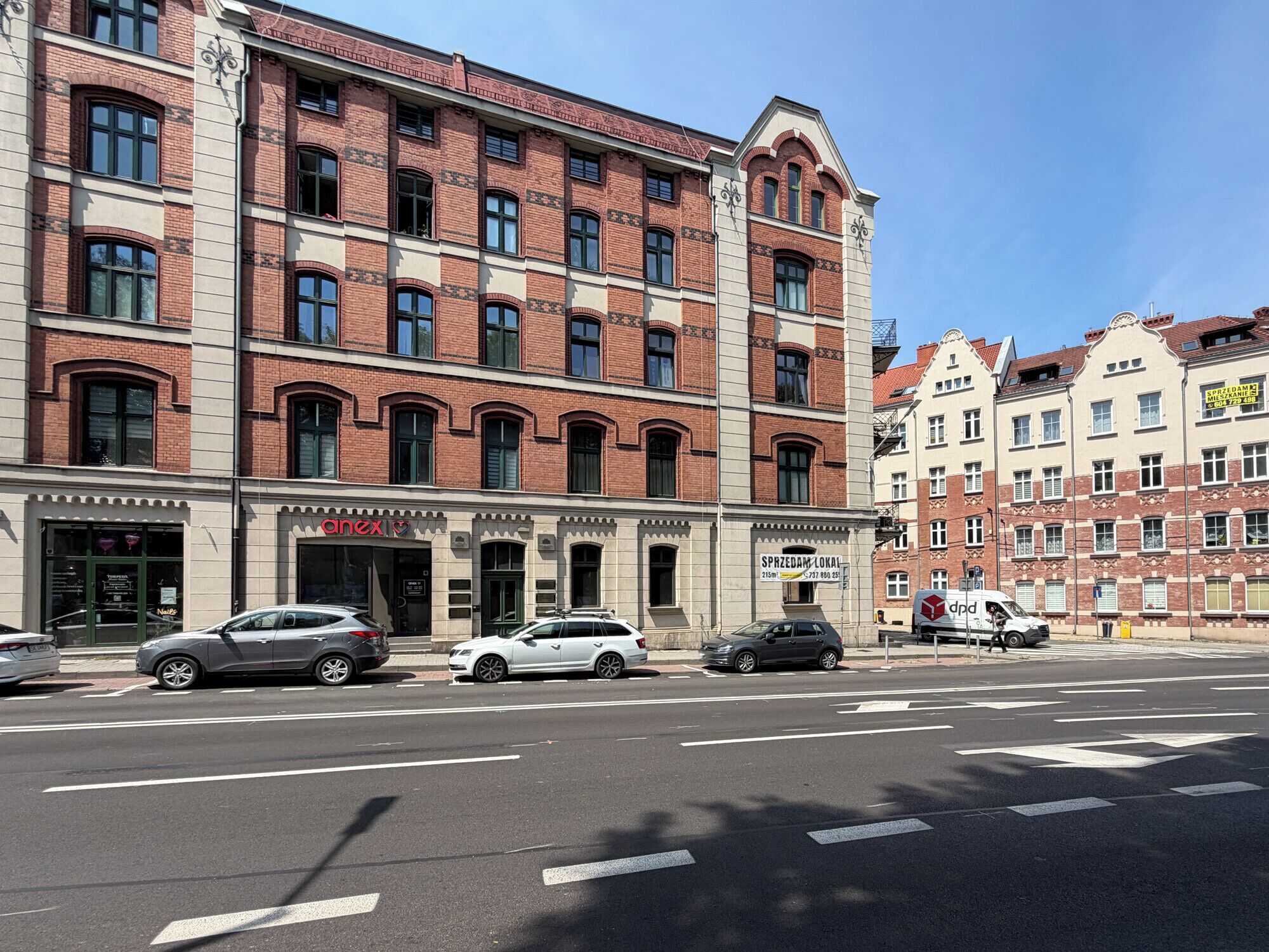 A multi-story building with a brick facade, a storefront with a sign, and parked cars on the street.