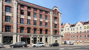 Ein mehrgeschossiges Gebäude mit Ziegelaußenwand, ein Laden mit Schaufenster und parkende Autos auf der Straße.