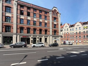 A multi-story building with a brick facade, a storefront with a sign, and parked cars on the street. - Mikołowska Silesian Charm Apartment (Katowice)